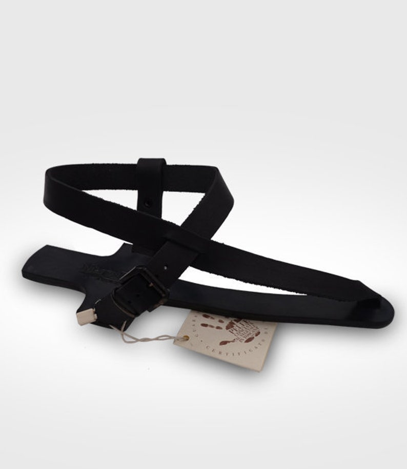 May include: Black leather sandals with a buckle fastening and a tag that says "Fair Trade Certified".