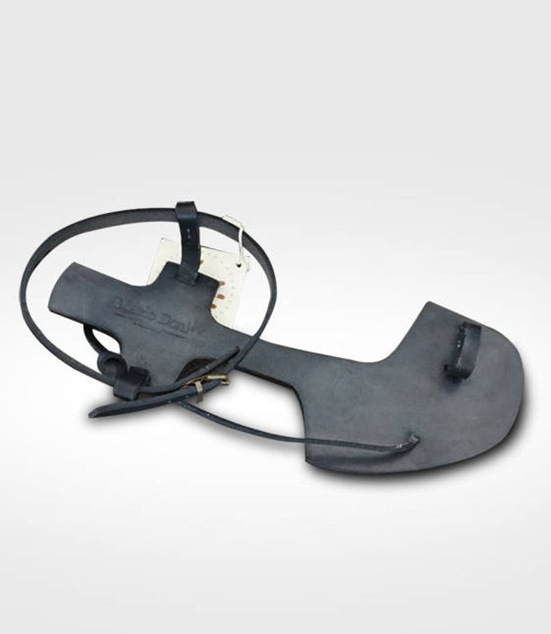May include: Black leather sandals with a strap that goes around the ankle and a buckle closure. The sandals have a simple design and are made of high-quality leather.