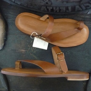 May include: Two pairs of brown leather sandals with buckle closures. The sandals have a simple design and are made of high-quality leather.