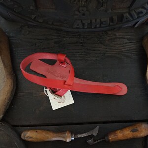 May include: Red leather sandal with a strap across the foot and a buckle fastening. The sandal is handmade and has a tag that says "Made to Order".