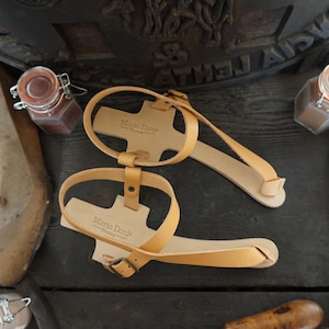 May include: A pair of tan leather sandals with adjustable straps and buckles. The sandals have the text "Mario Deni" printed on the straps.