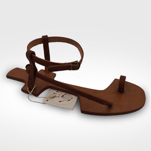 May include: Brown leather sandals with a single strap that goes around the ankle and a toe loop. The sandals have a simple design and are made of high-quality leather.