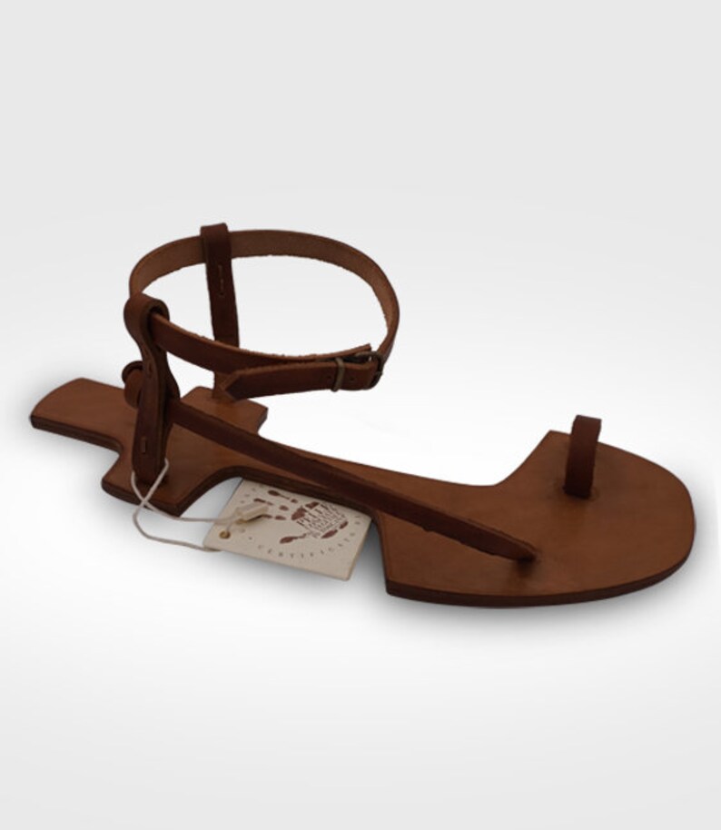 May include: Brown leather sandals with a single strap that goes around the ankle and a toe loop. The sandals have a simple design and are made of high-quality leather.