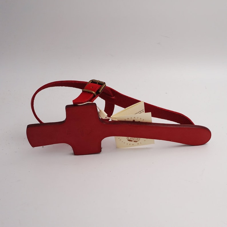 May include: Red leather sandal with a cross-shaped strap and a buckle fastening. The sandal is on a white background.