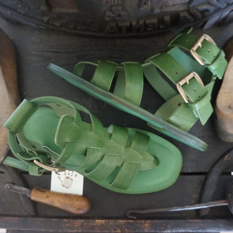 May include: A pair of green leather sandals with buckle closures. The sandals have a gladiator style with multiple straps.