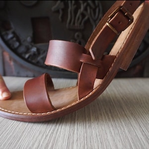 May include: Brown leather sandals with a buckle strap and a stitched sole.