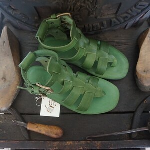 May include: A pair of green leather sandals with a buckle closure. The sandals have a woven design and are made of a soft, supple leather.