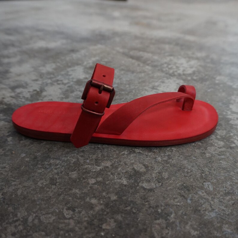 May include: Red leather sandals with a buckle strap and a toe loop.