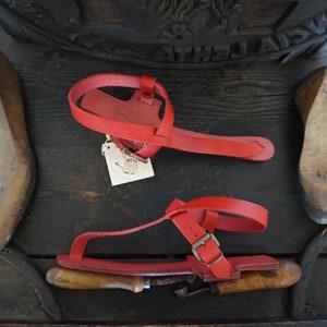 May include: A pair of red leather sandals with a buckle strap. The sandals are handmade and have a wooden sole.