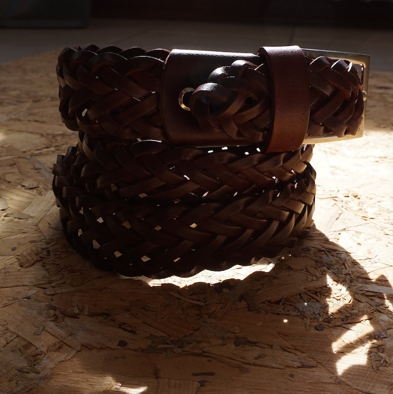 Puede incluir: Un cintur&oacute;n de cuero marr&oacute;n con un dise&ntilde;o trenzado. El cintur&oacute;n tiene una hebilla plateada y un nudo tejido en el extremo.