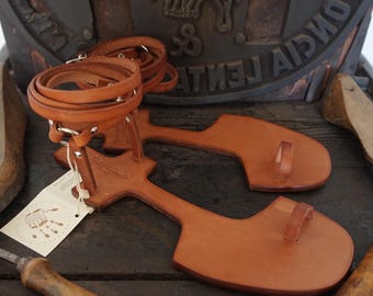Può includere: Un paio di sandali in pelle marrone con un design semplice. I sandali hanno un unico cinturino che si avvolge intorno alla caviglia e un passante per le dita. I sandali sono realizzati in pelle di alta qualità e sono perfetti per l'estate.