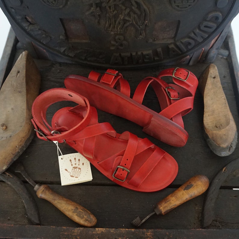 K&ouml;nnte beinhalten: Zwei Paar rote Ledersandalen mit Schnallenverschl&uuml;ssen. Die Sandalen haben ein schlichtes Design mit mehreren Riemen.