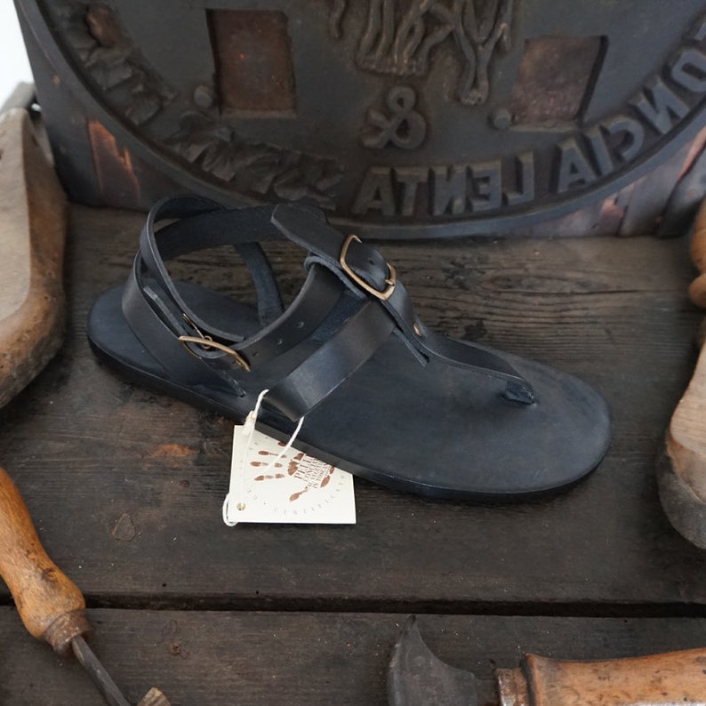 Pu&ograve; includere: Sandali in pelle nera con chiusura a fibbia e un'etichetta in pelle marrone che dice "Handmade with Love".