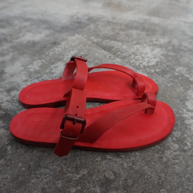 May include: A pair of red leather sandals with a buckle strap and a thong style toe strap.
