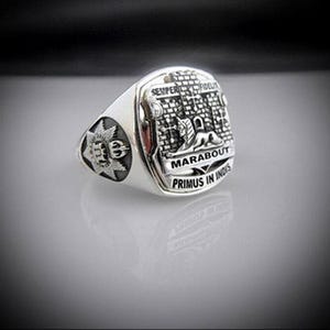 Op de afbeelding: Een zilveren ring met een wapenschild met een kasteel, een leeuw en de woorden "Marabout Primus in Indis".