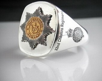 May include: A silver ring with a raised design of a starburst with a smaller circle in the center. The starburst is silver and the circle is gold. The text "The Cheshire Regiment" is inscribed in the circle. The text "22nd Cheshire Regiment" is inscribed on the band of the ring.