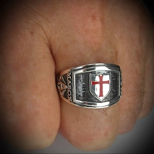Könnte beinhalten: Ein silberner Ring mit einem Schild-Design, das ein rotes Kreuz zeigt. Der Ring ist mit dem Wort "MASON" graviert.