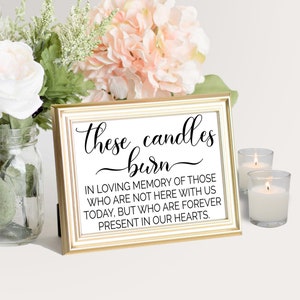 May include: A gold-framed sign with the text "these candles burn" in black cursive lettering. The sign also includes the text "In loving memory of those who are not here with us today, but who are forever present in our hearts."