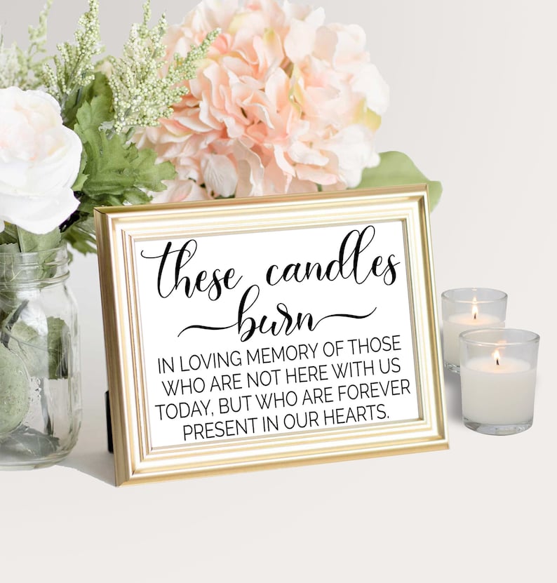 May include: A gold-framed sign with the text "these candles burn" in black cursive lettering. The sign also includes the text "In loving memory of those who are not here with us today, but who are forever present in our hearts."