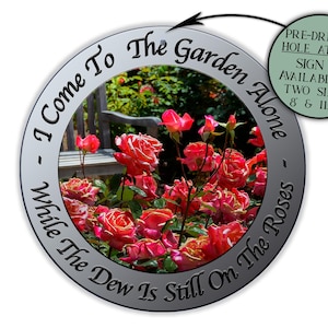 May include: A round metal sign with a silver background and black text. The sign features a picture of a garden with pink roses and a wooden bench. The text on the sign reads: "I Come To The Garden Alone - While The Dew Is Still On The Roses". The sign is available in two sizes: 8 inches and 11.75 inches.