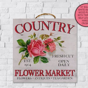 May include: A square, white-washed wood plaque with a twine hanger. The sign features the word "COUNTRY" in red, along with a floral illustration of pink roses and green leaves. Text includes "FRESH CUT", "OPEN DAILY", and "FLOWER MARKET".