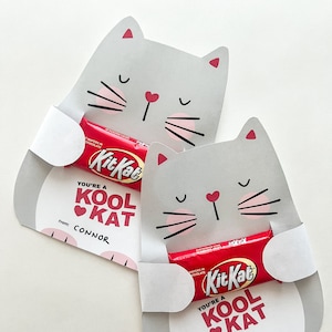 Peut inclure: Deux porte-cartes en forme de chat gris avec des accents roses. Chaque porte-cartes contient une barre de chocolat Kit Kat et un message qui dit "You're a Kool Kat". Le premier porte-cartes porte le nom "Connor" sous le message. Le deuxième porte-cartes porte le nom "Julie" sous le message.