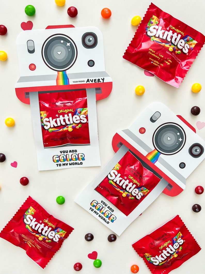 May include: A printable Valentine's Day card with a Skittles candy packet inside. The card is shaped like an instant camera and has the text "You add color to my world" on it. The card is decorated with rainbow colors.