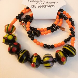 May include: A 25-inch Halloween Goosebumps necklace with black and orange beads. The necklace features a variety of black and yellow glass beads with different patterns.