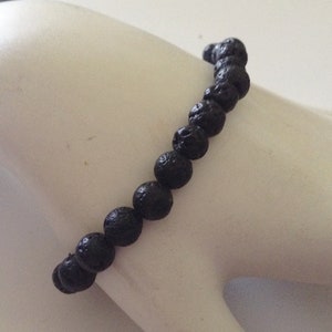 May include: A black lava rock beaded bracelet. The bracelet is made of small, round beads that are strung together on a black elastic cord.