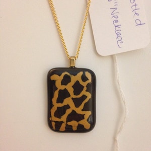 May include: Gold chain necklace with a black and gold rectangular pendant featuring a spotted pattern. The tag reads "Spotted 18" Necklace".