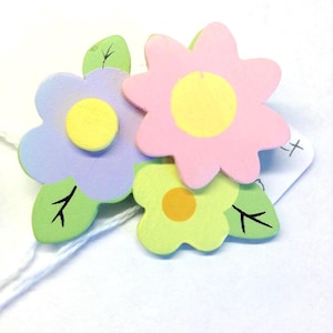 May include: Three wooden flowers with painted details. The flowers are pink, purple, and green. The flowers have yellow centers.