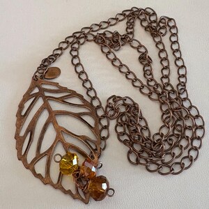 May include: A copper necklace with a leaf-shaped pendant and amber-colored glass beads. The chain is a simple link style.