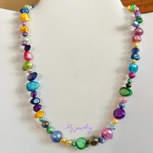 May include: A colorful necklace made of iridescent, multi-colored beads. The necklace is made of various shapes and sizes of beads, including round, oval, and teardrop shapes. The beads are strung on a silver chain.
