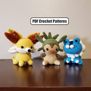 May include: Three crocheted stuffed toys, a yellow fox with orange ears, a brown bird with green leaves on its head, and a blue frog with white accents. The toys are arranged on a wooden surface. PDF Crochet Patterns.