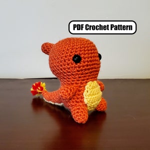 Puede incluir: Un personaje de Pokemon de crochet naranja y amarillo con ojos negros. El personaje está de pie sobre una superficie de madera marrón. Patrón de crochet PDF.