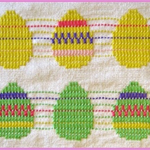 May include: A white fabric with a repeating pattern of embroidered eggs in yellow, green, and purple. The eggs are outlined in yellow, green, and purple thread. The eggs are arranged in two rows of three.