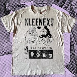 Könnte beinhalten: Weißes T-Shirt mit einem schwarzen Aufdruck eines Cartoon-Hundes und einer Ente mit dem Text "KLEENEX Liliput Die Matrosen" und einem kleinen Anker.