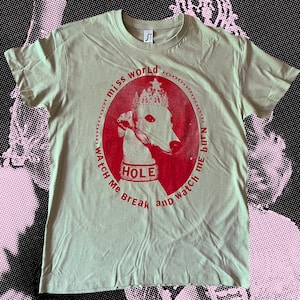 Könnte beinhalten: Hellgrünes T-Shirt mit roter Grafik eines Hundes mit Krone und Halsband mit der Aufschrift "HOLE". Der Text um den Hund lautet "miss world watch me burn and watch me break".