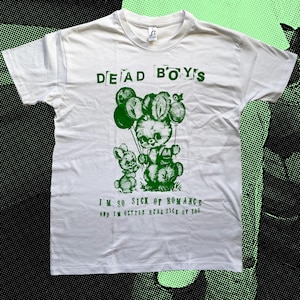May include: White t-shirt with green text and graphic. The text reads "DEAD BOYS" above a green illustration of two bunny-like creatures holding balloons. Below the graphic, the text reads "I'M SO SICK OF ROMANCE and I'M GETTIN' REAL SICK OF YOU."