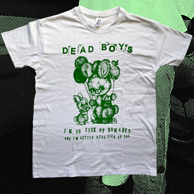 May include: White t-shirt with green text and graphic. The text reads "DEAD BOYS" above a green illustration of two bunny-like creatures holding balloons. Below the graphic, the text reads "I'M SO SICK OF ROMANCE and I'M GETTIN' REAL SICK OF YOU."
