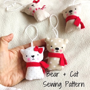 May include: Handmade bear and cat ornaments with red scarves and bows. The bear ornaments have a beige polka dot pattern, while the cat ornaments have a white polka dot pattern. The text "Bear + Cat Sewing Pattern" is visible.