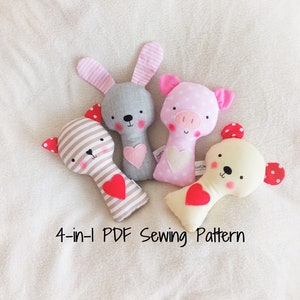 May include: Four plush rattle toys in the shapes of a bunny, pig, bear, and cat. The toys are made of soft fabrics and have embroidered faces. Each toy has a red heart-shaped rattle inside. The toys are arranged on a white fluffy surface. The text "4-in-1 PDF Sewing Pattern" is written below the toys.