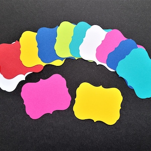 May include: A set of 12 colorful paper tags with a scalloped edge. The tags are arranged in a semi-circle and are in various colors, including red, yellow, blue, green, pink, and turquoise.