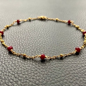 May include: A gold chain anklet with red gemstone beads.