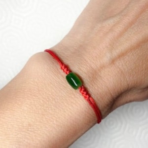 May include: A red string bracelet with a single green jade bead.