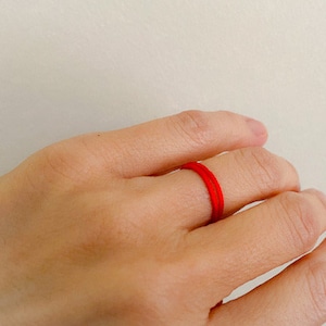May include: A red string bracelet worn on a person's finger.