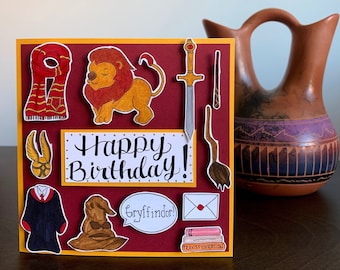 May include: A red and gold card with a lion, a wand, a sword, a scarf, a hat, a book, a letter, and a robe. The card says "Happy Birthday!" and "Gryffindor!"