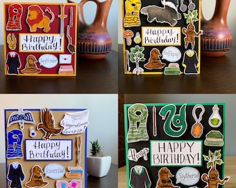 May include: Four handmade greeting cards with a Harry Potter theme. Each card features a different Hogwarts house: Gryffindor, Hufflepuff, Ravenclaw, and Slytherin. The cards are decorated with various Harry Potter-themed illustrations, including a lion, a badger, an eagle, and a snake.
