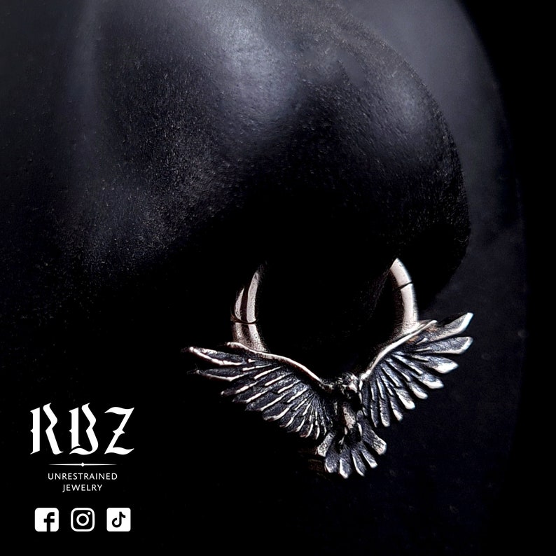 A highly detailed, Gothic crow / raven shaped clicker septum ring, made from solid Sterling silver, by RBZ Jewelry, displayed on a nose.
