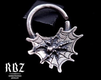 May include: A silver hoop earring featuring a textured spider web design with a small spider at the center. The piece is labeled as solid sterling silver and includes the text RBZ UNRESTRAINED JEWELRY with social media icons.